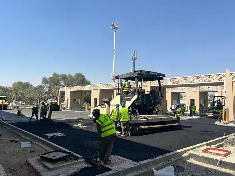Road infrastructure construction with asphalt paving machine and workers by Osool AlRoyah General Contracting in the UAE